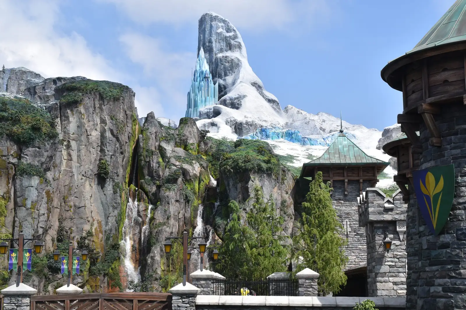 The Frozen Kingdom area of Fantasy Springs: an icy, snow-capped North Mountain above grey cliffs and a waterfall, with stone castle towers and pine trees in front